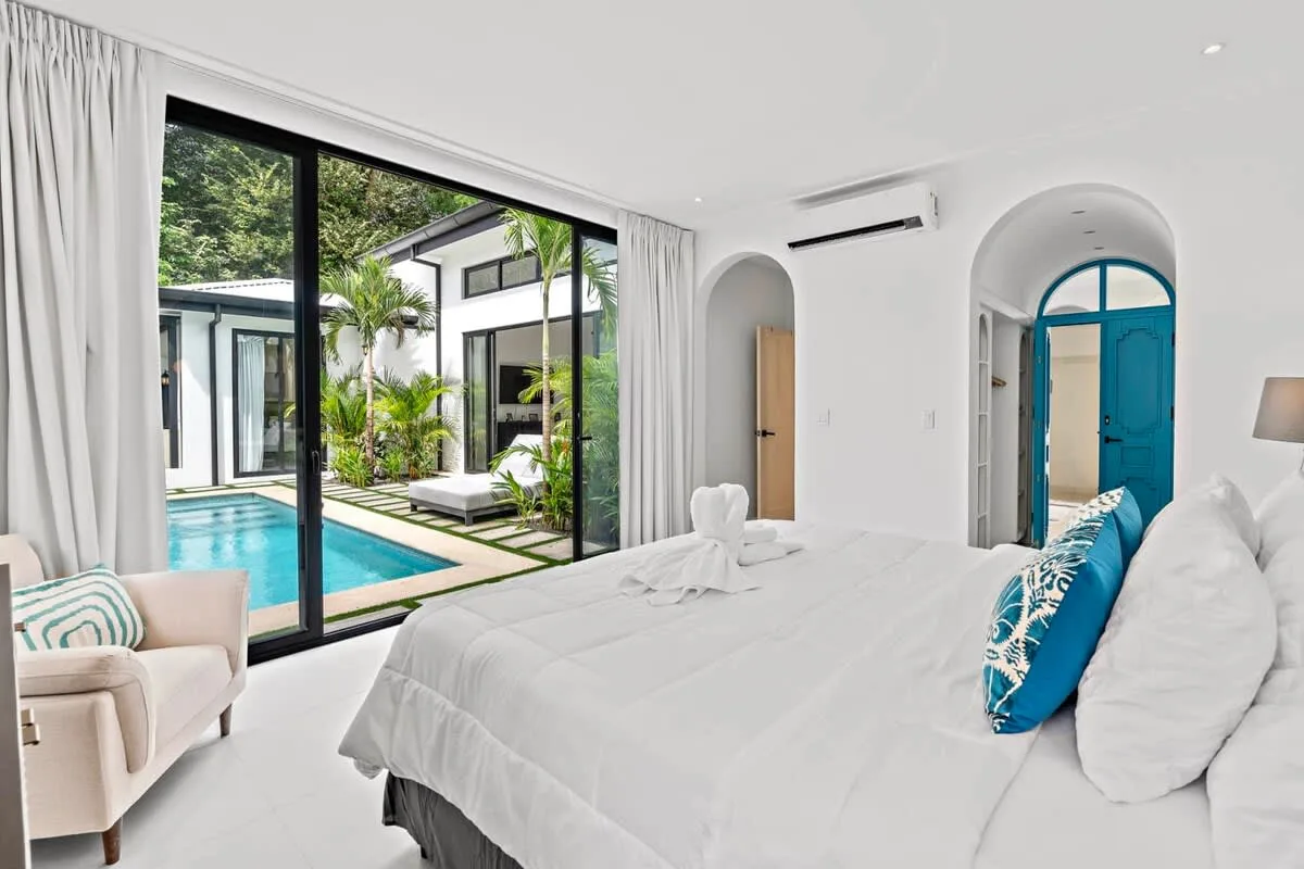 A bright bedroom opens onto a pool courtyard through wide glass doors.