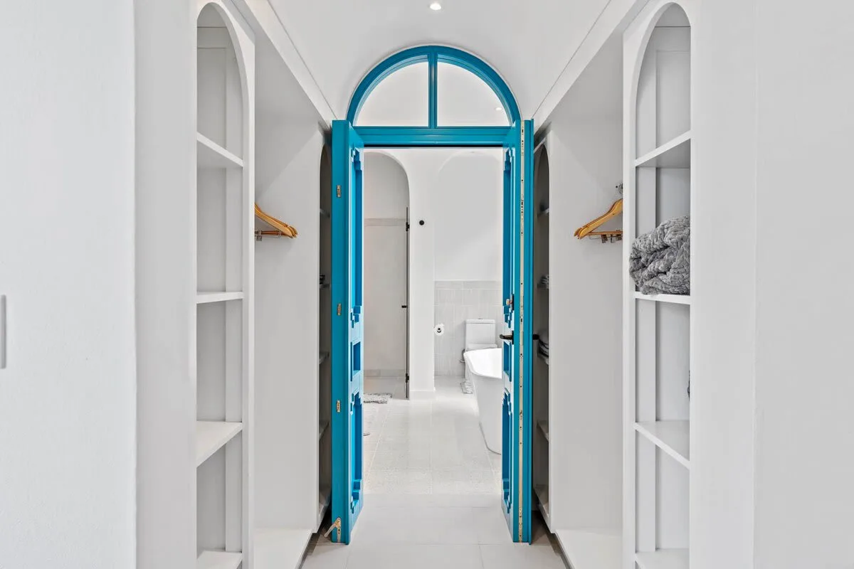 A bright white hallway leads through an open blue arched doorway into a bathroom.