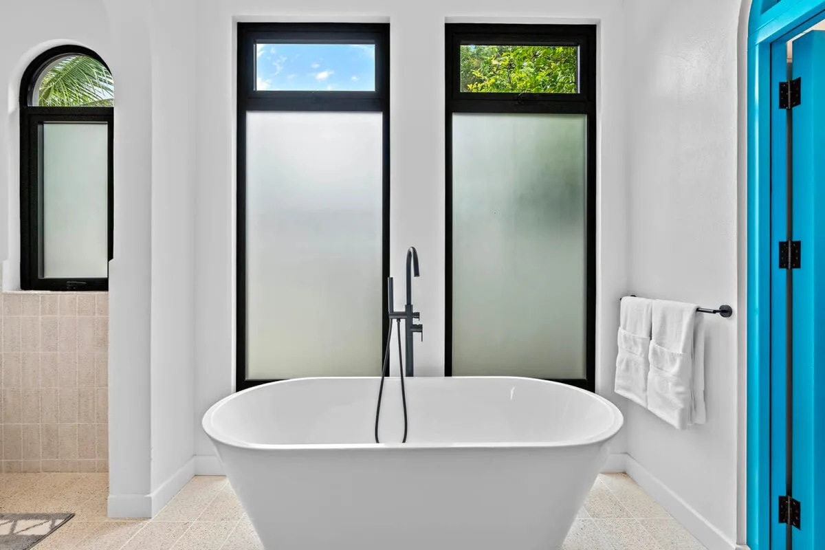 A bright bathroom with a freestanding bathtub beneath tall windows.