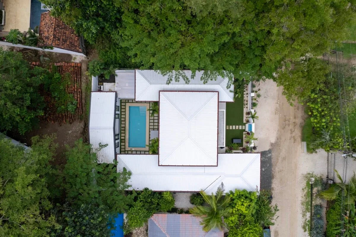An aerial view of a building with a rectangular swimming pool surrounded by greenery.