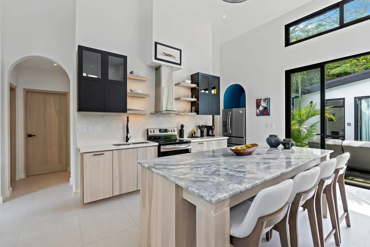 A bright kitchen with a large island and seating beside floor-to-ceiling windows.