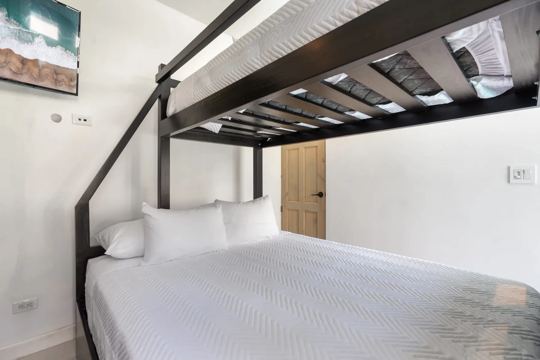 A bedroom with a white bed beneath a dark upper bunk.