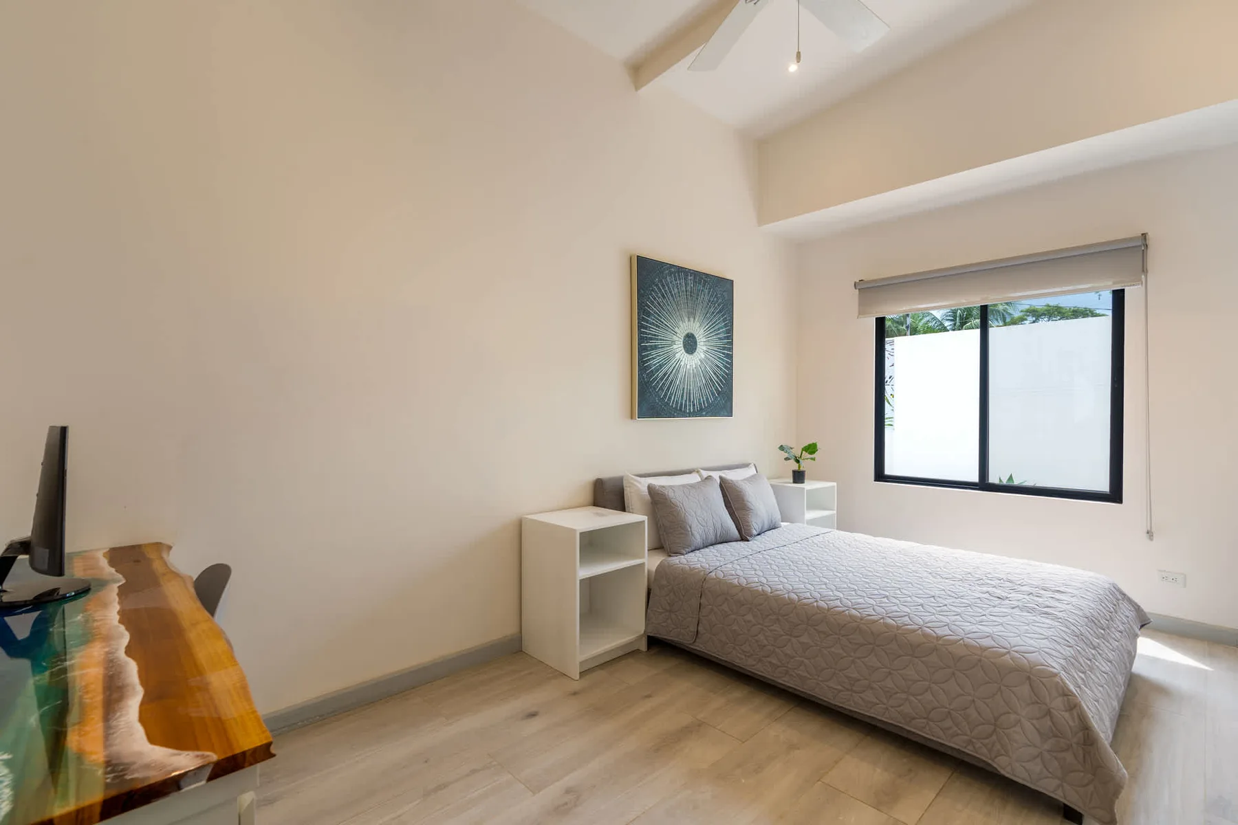 A bright bedroom with a bed beside a large window.