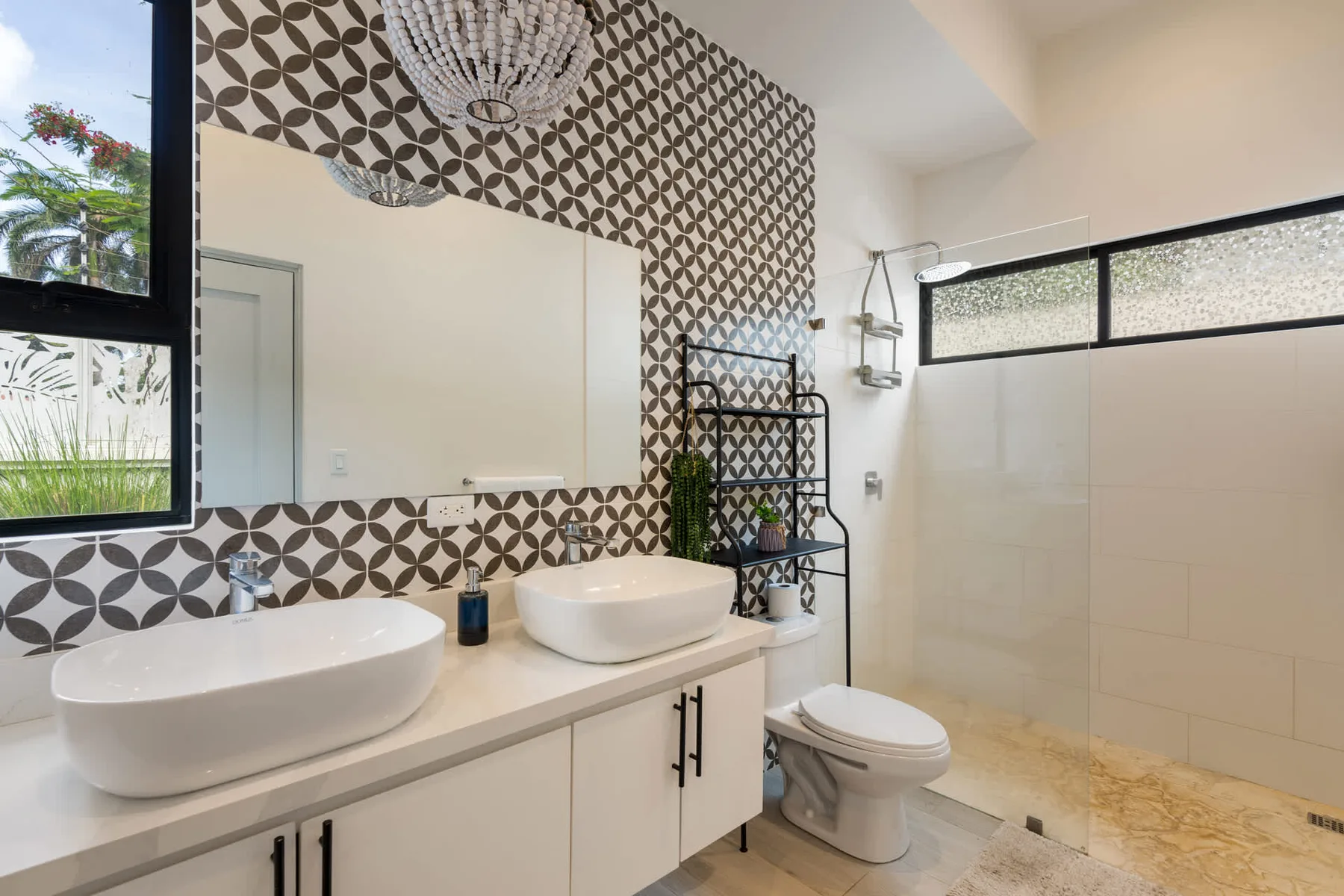 A bright bathroom with a double vanity, patterned tile, and a glass shower.
