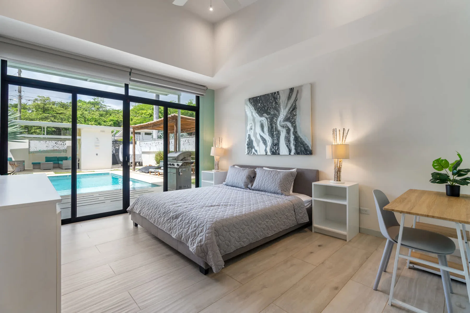 A bright bedroom with a bed beside large glass doors overlooking a pool.