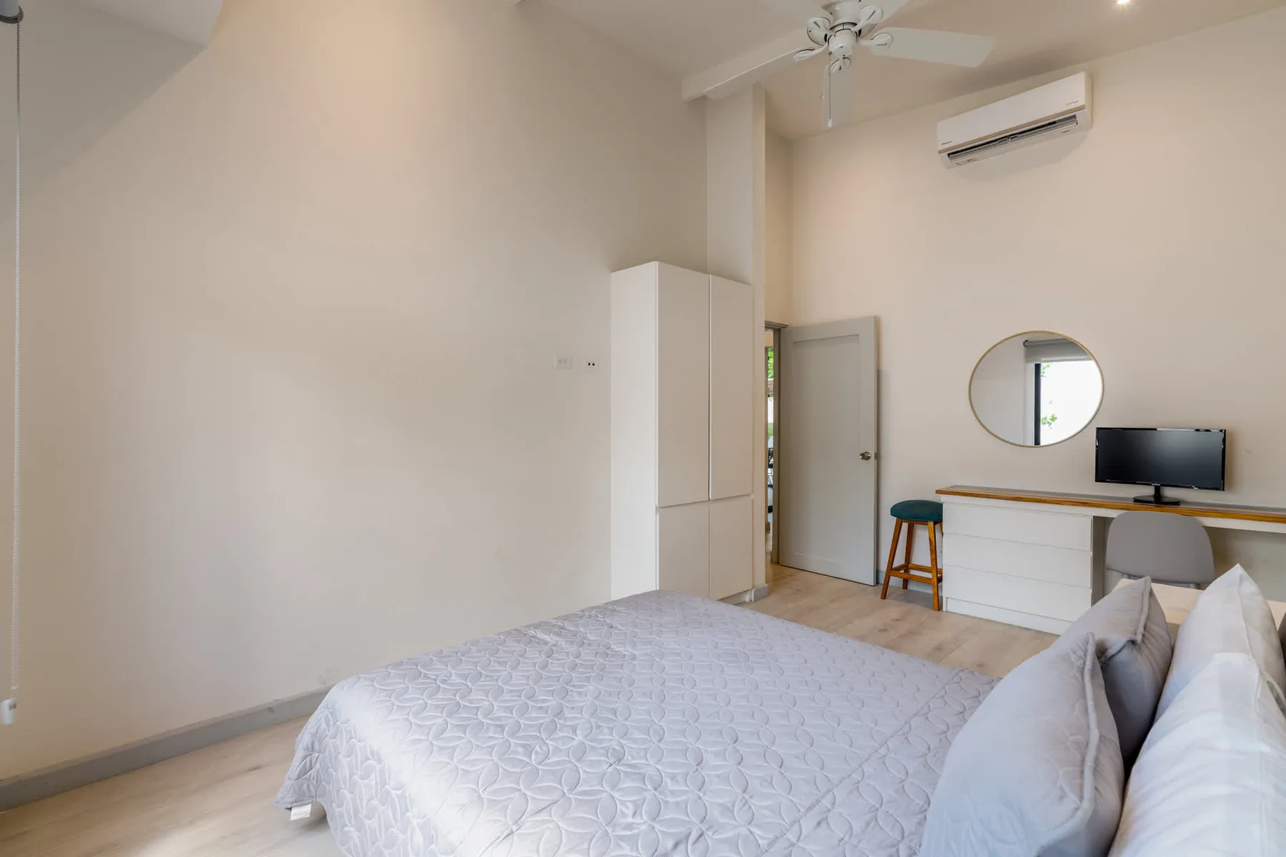 A bedroom with a bed, wardrobe, and a desk beneath a round mirror.