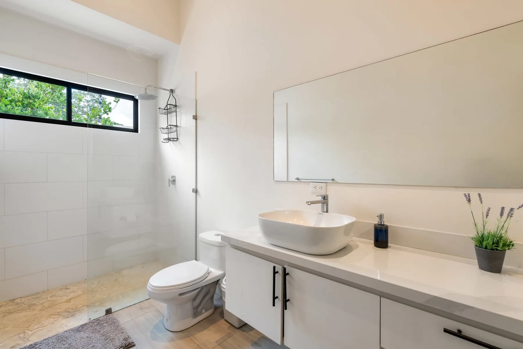 A bright bathroom with a long vanity, large mirror, and walk-in shower.