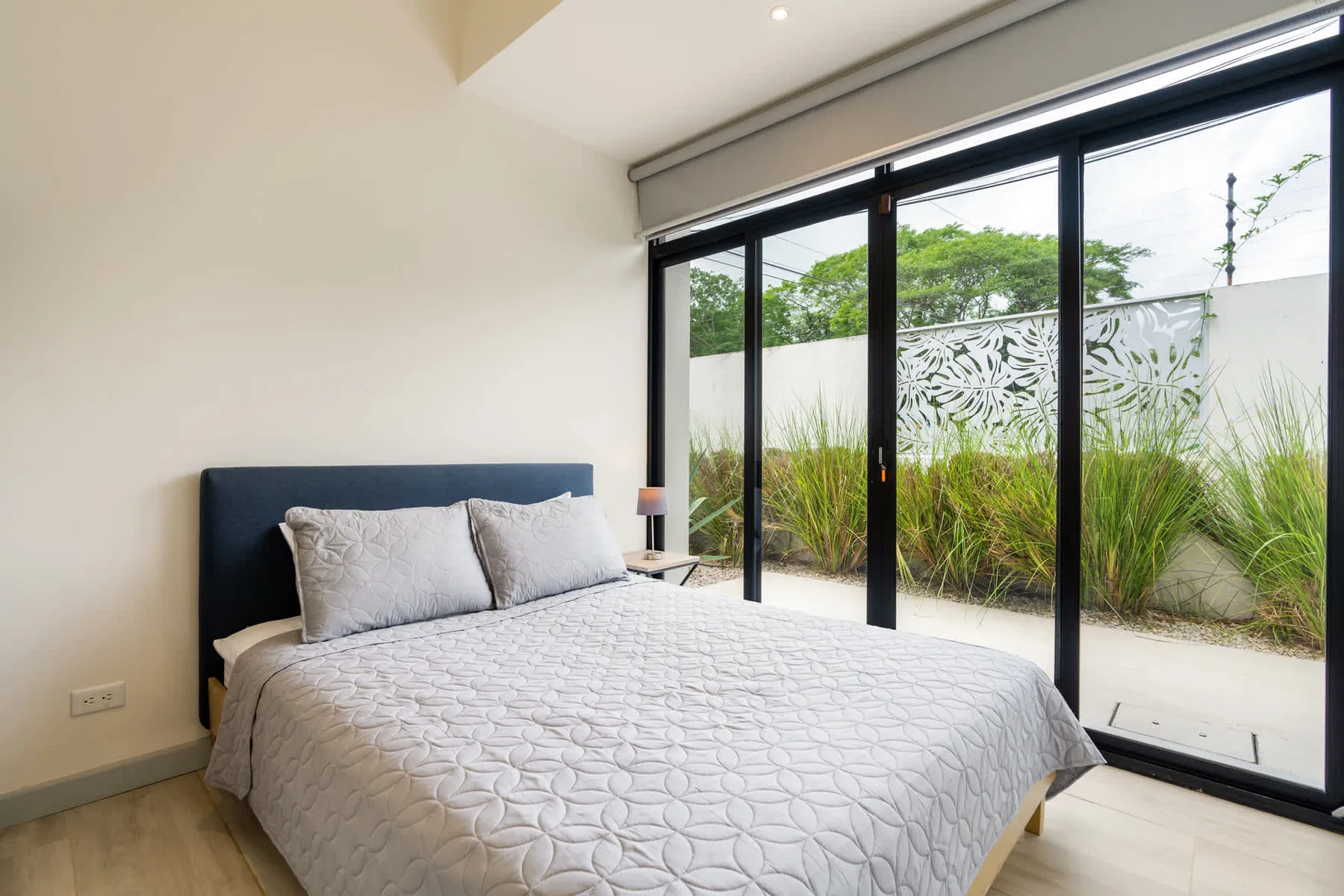 A bedroom with a bed beside large glass doors opening onto a planted patio.