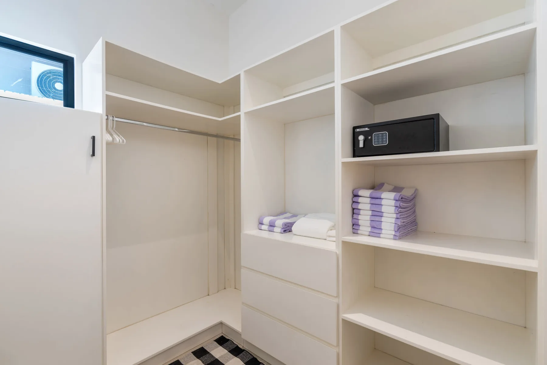 A walk-in closet with open shelving, folded towels, and a small safe.