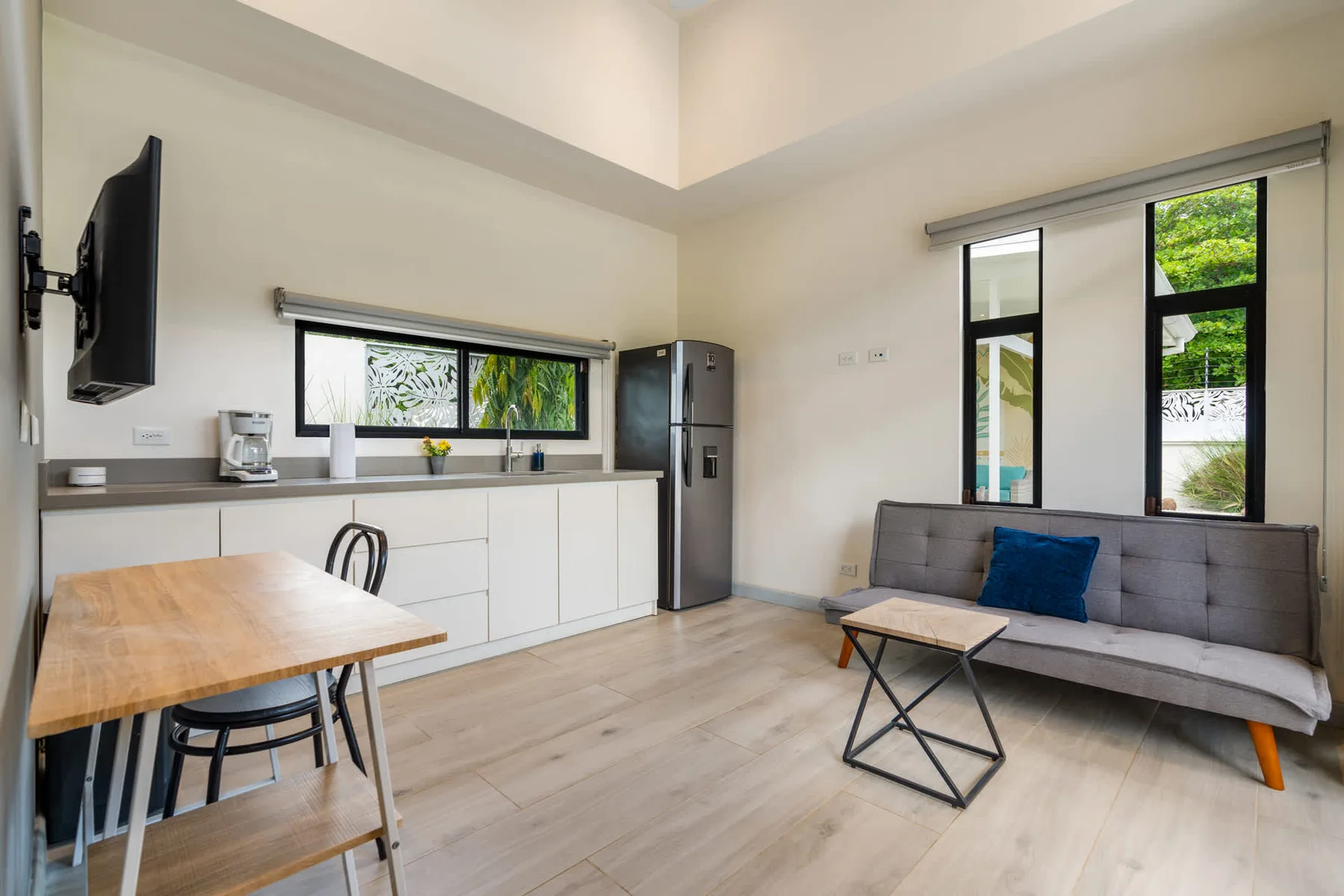 A bright open-plan living and kitchen area with a dining table and gray seating.