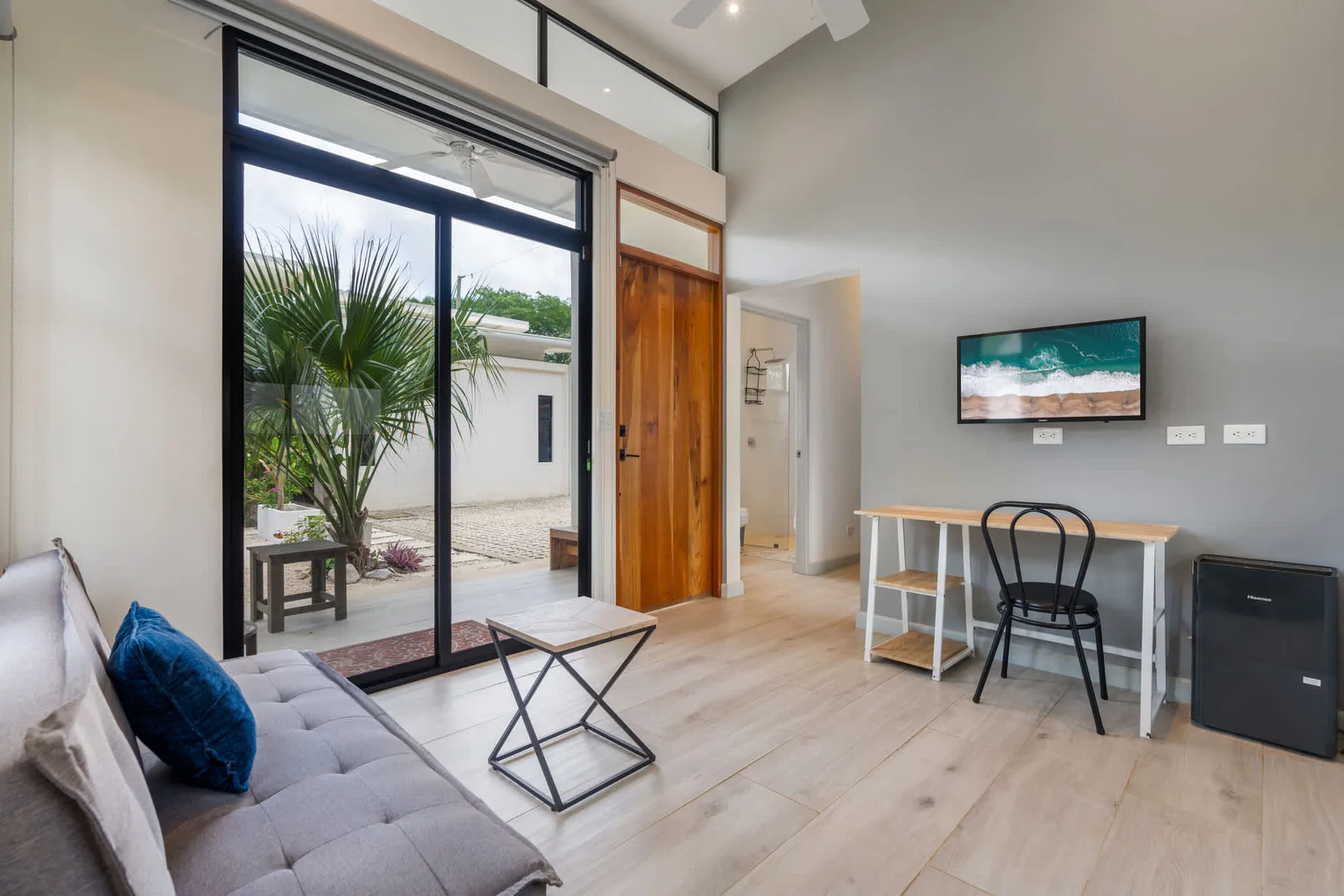 A bright living area with seating, a small table, and a desk by sliding glass doors.