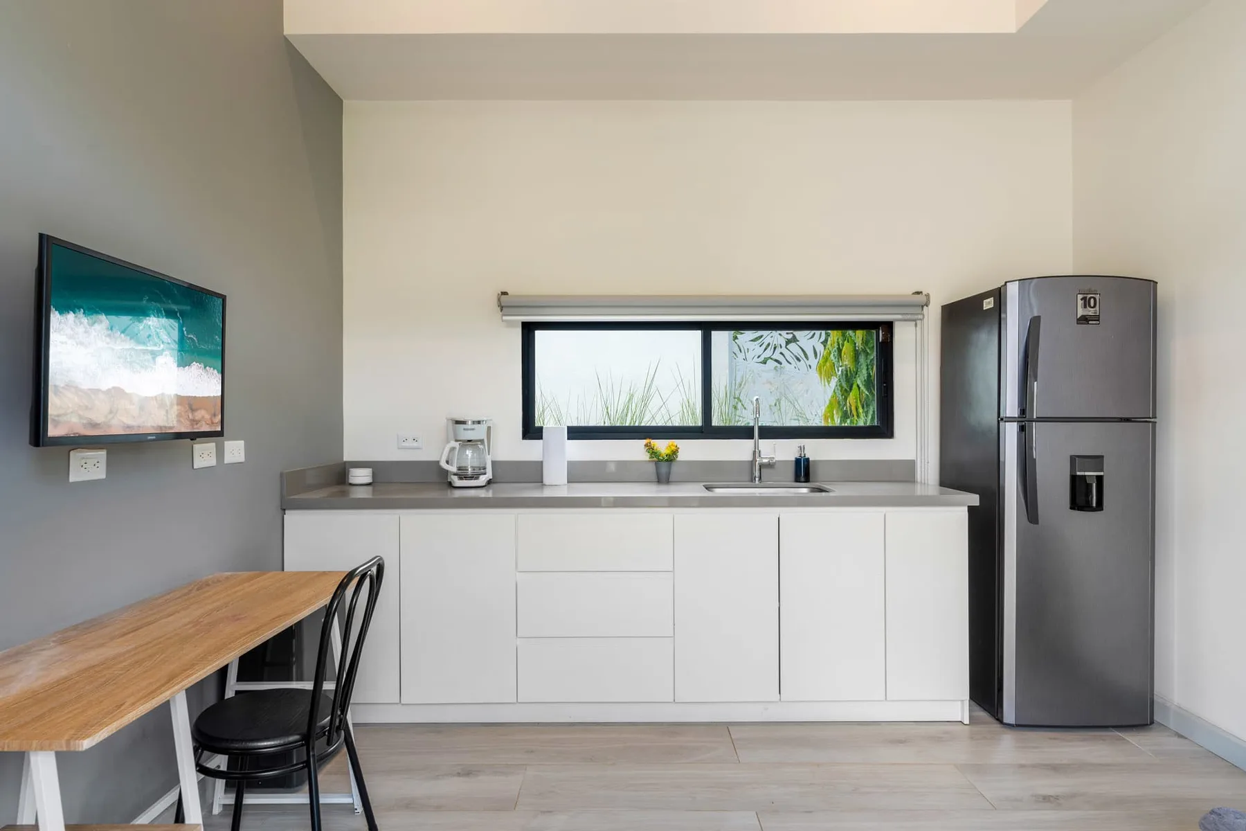 A modern kitchen with white cabinets, a countertop, and a window above the sink.
