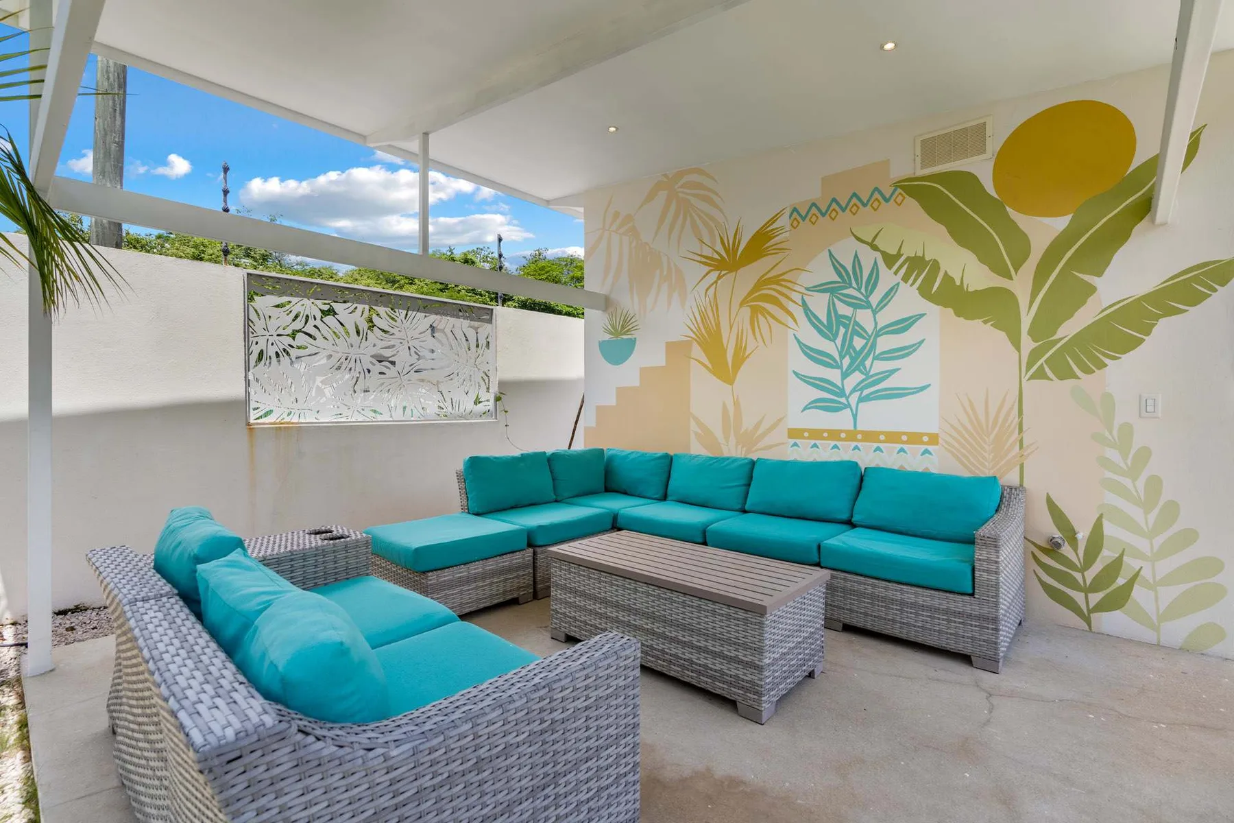 An outdoor lounge with teal seating and a large botanical mural.
