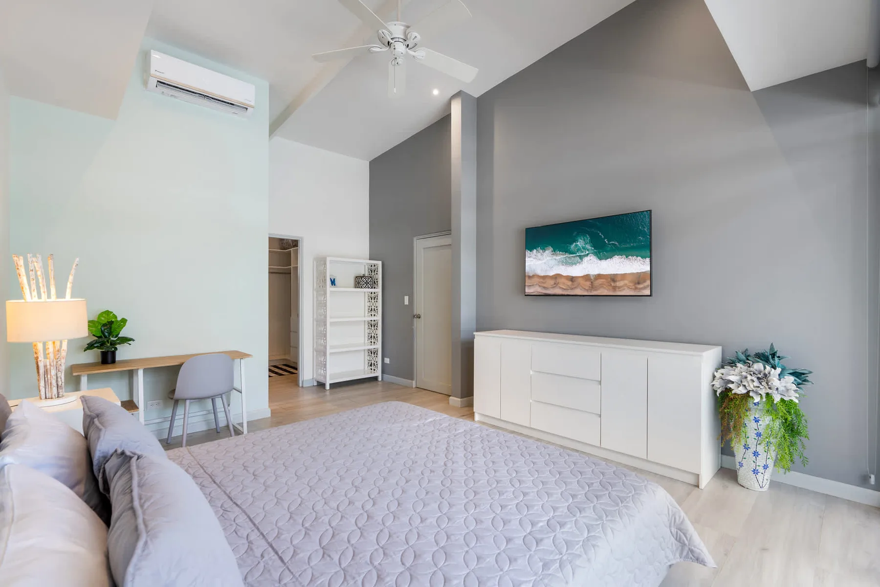 A bright bedroom with a large bed, white dresser, and ocean artwork.