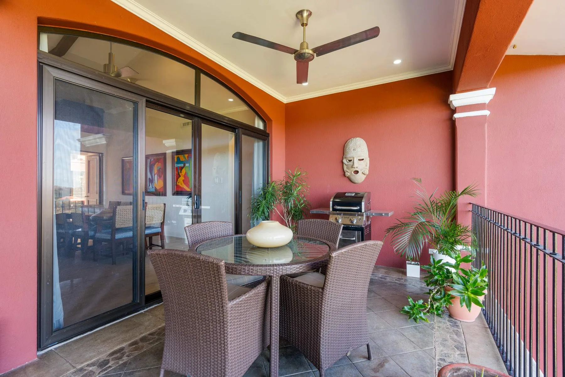 Un patio cubierto con una mesa de vidrio, asientos tejidos y plantas en macetas.