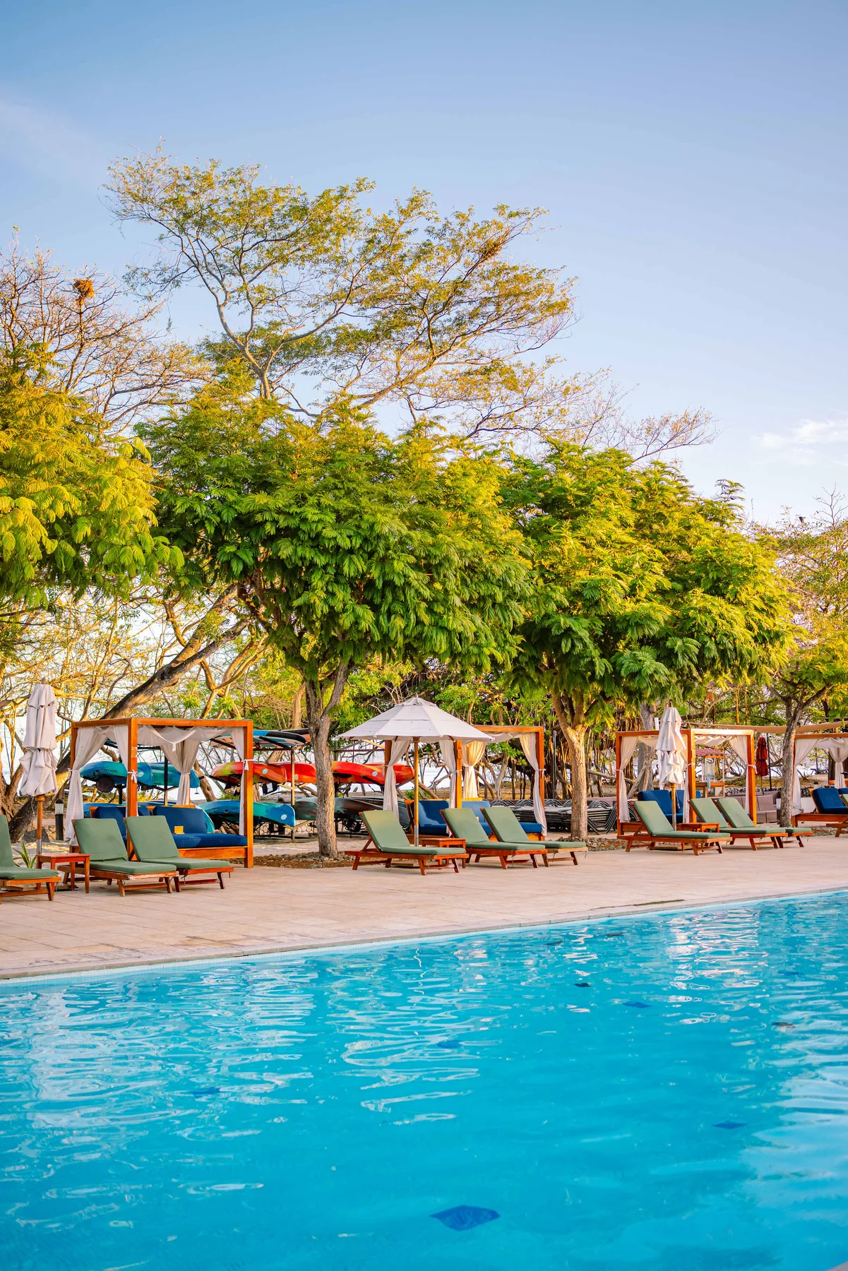 Zona común: Zona de asientos junto a la piscina, a la sombra de árboles frondosos.