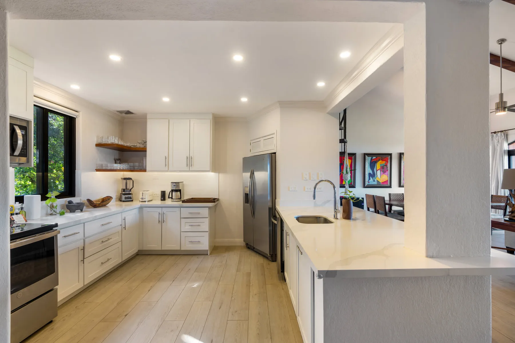 Una cocina luminosa con gabinetes blancos, electrodomésticos de acero inoxidable y una isla larga.