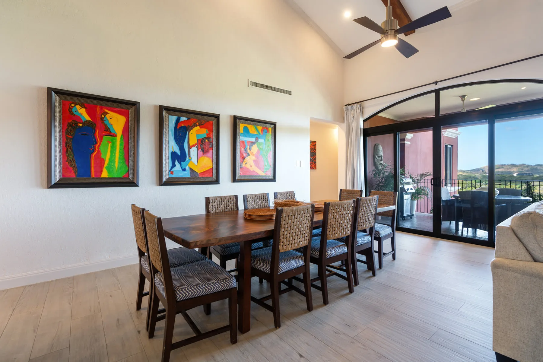 Un comedor con una mesa larga de madera, asientos estampados y obras de arte coloridas.