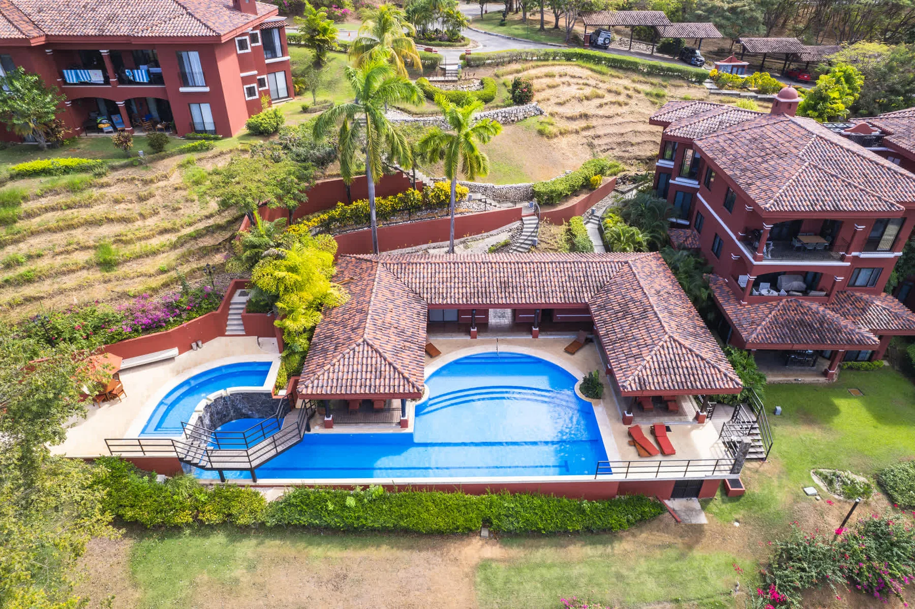Zona común: Una piscina al aire libre está rodeada de jardines y edificios con techos rojos.