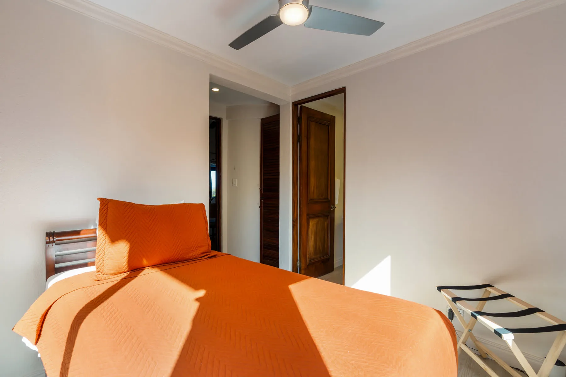 Dormitorio con una colcha naranja, una puerta de madera y un ventilador de techo.