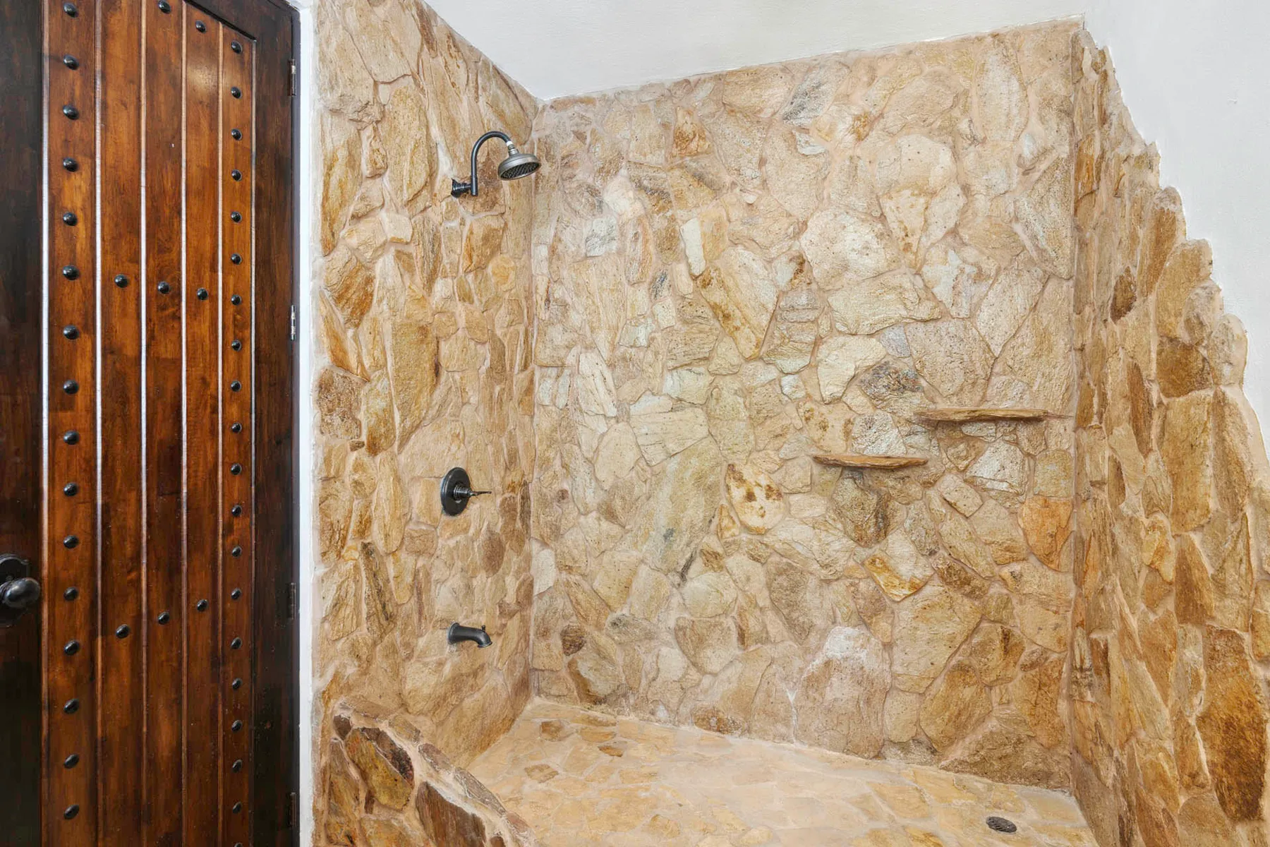 A stone shower area with a wooden door and wall-mounted shower fixtures.