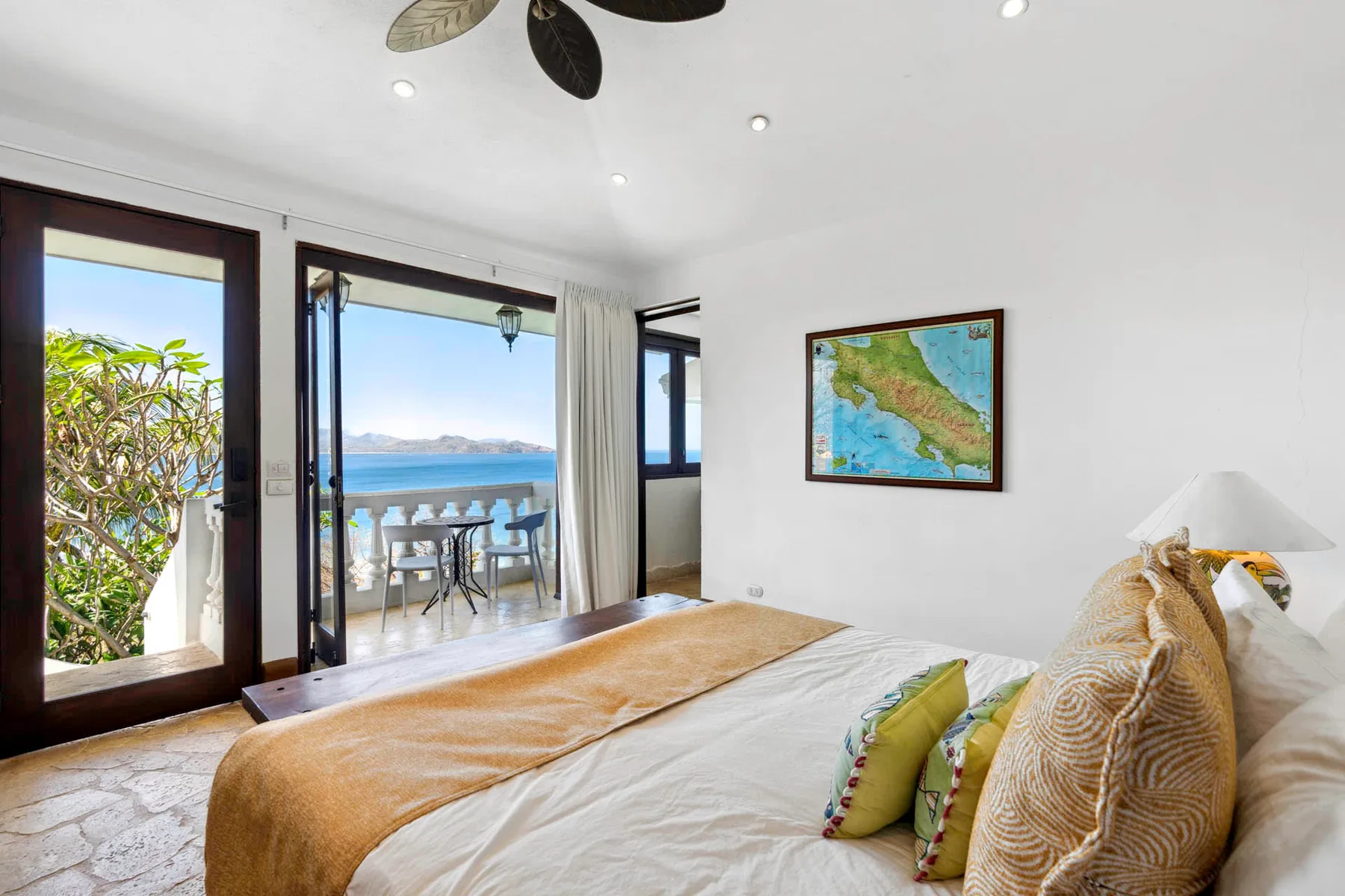 A bedroom opens onto a balcony with seating and a view of the water.