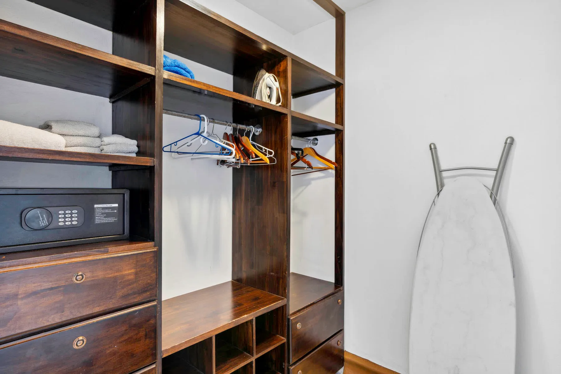 A built-in wardrobe with open shelves, hanging space, and an ironing board.