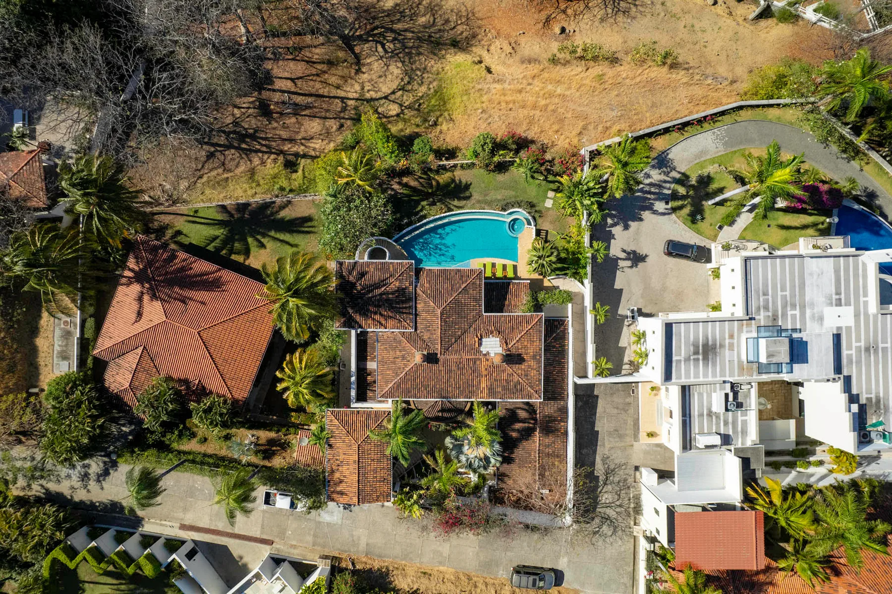 Aerial view of a residential property with a turquoise swimming pool and surrounding gardens.