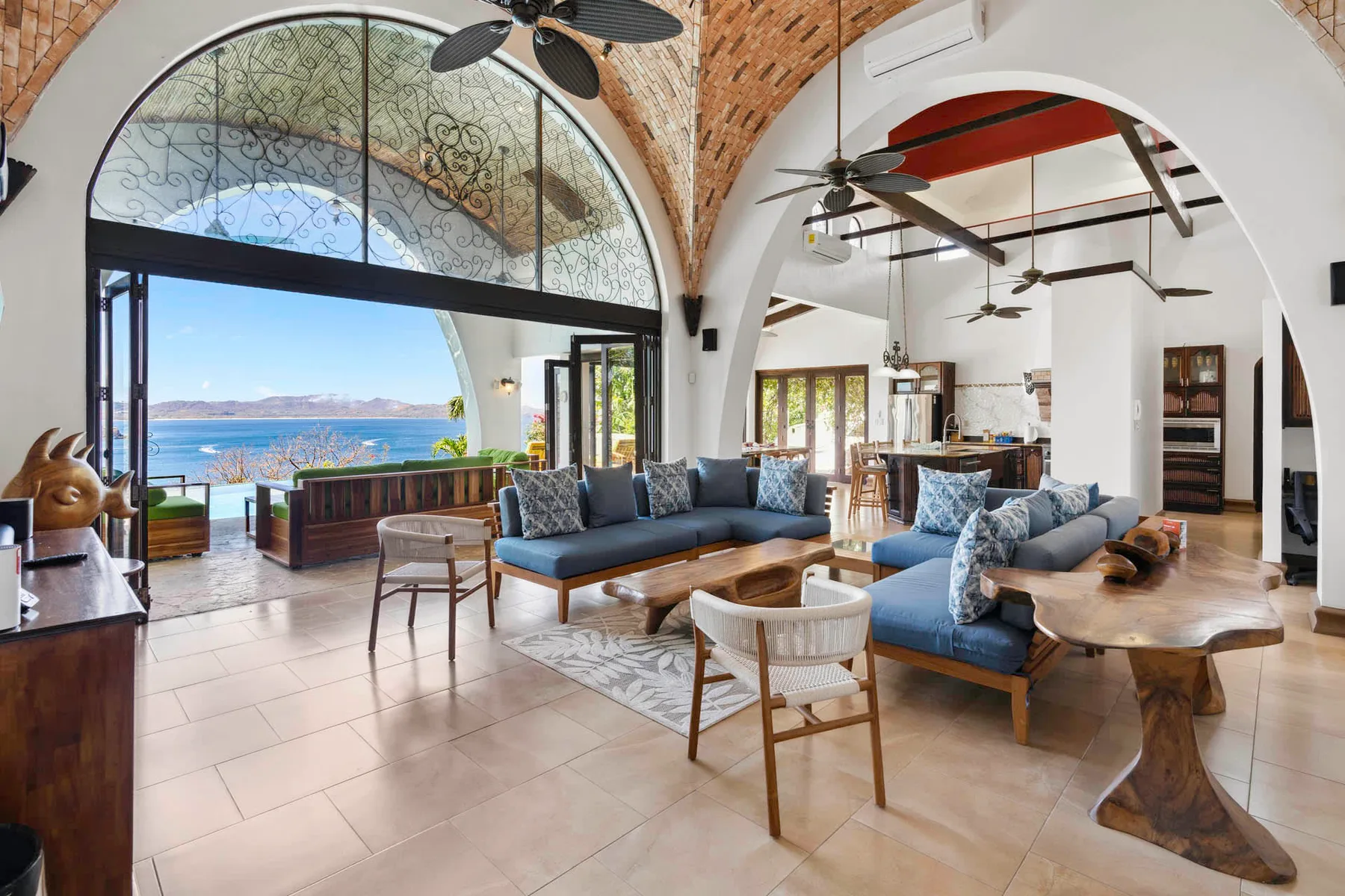 A spacious living room with blue seating and large arched windows overlooking the water.