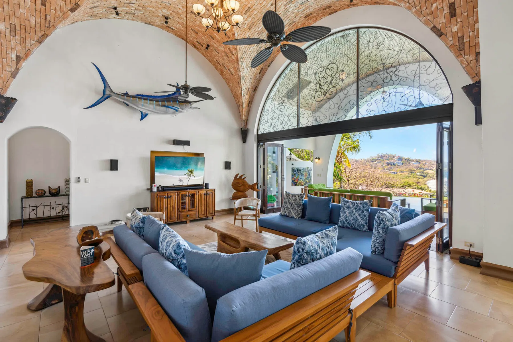 A spacious living room with blue seating and large arched windows overlooking the landscape.