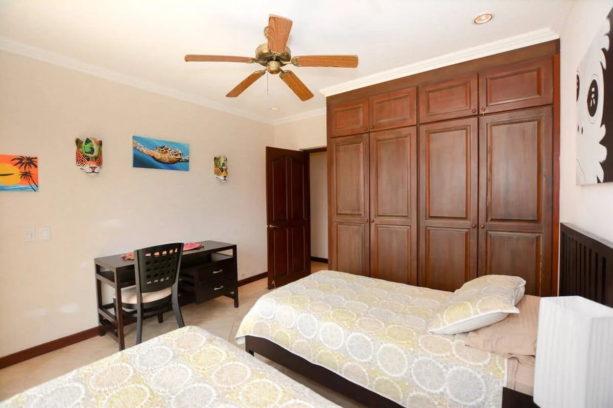 A bedroom with patterned bedding, a ceiling fan, and a large wooden wardrobe.