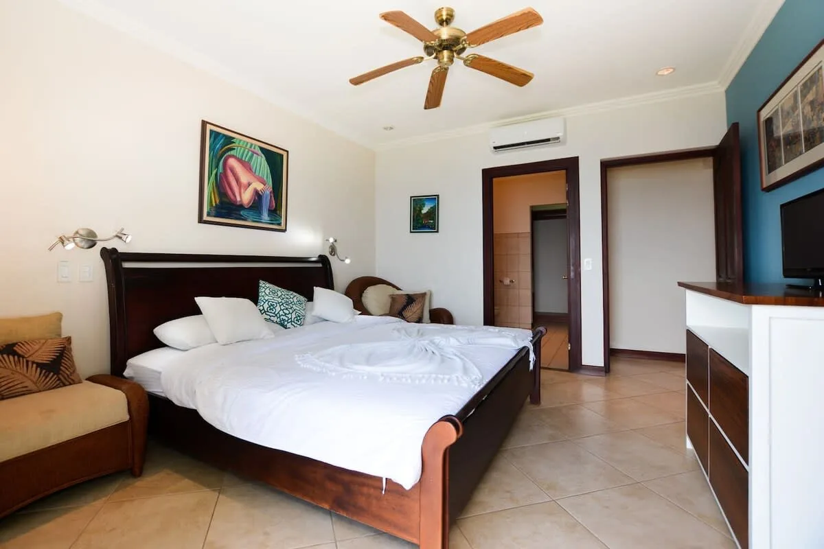 A bedroom with a large bed, framed artwork, and a ceiling fan.