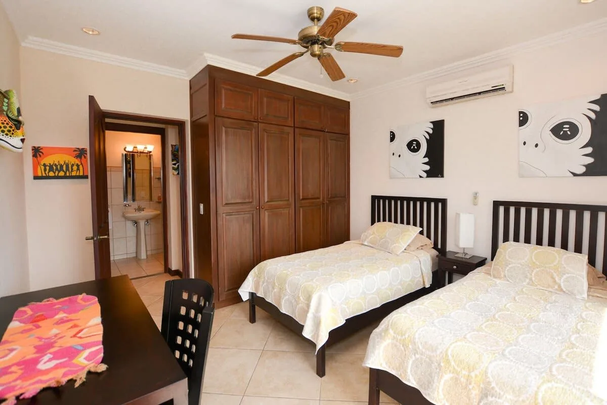 A bedroom with two beds, dark wood wardrobes, and a ceiling fan.