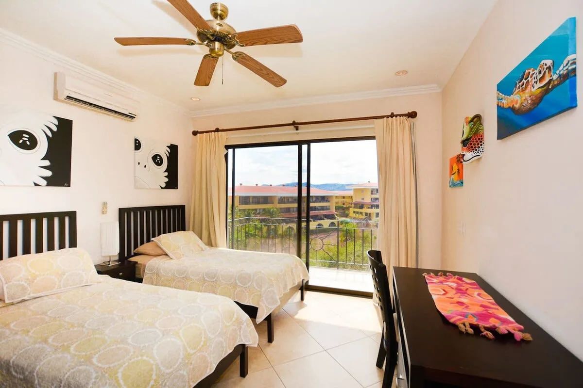 A bedroom with two beds, a ceiling fan, and sliding glass doors.