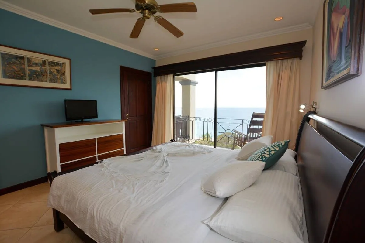 A bedroom with a bed, a television, and glass doors opening onto a balcony.