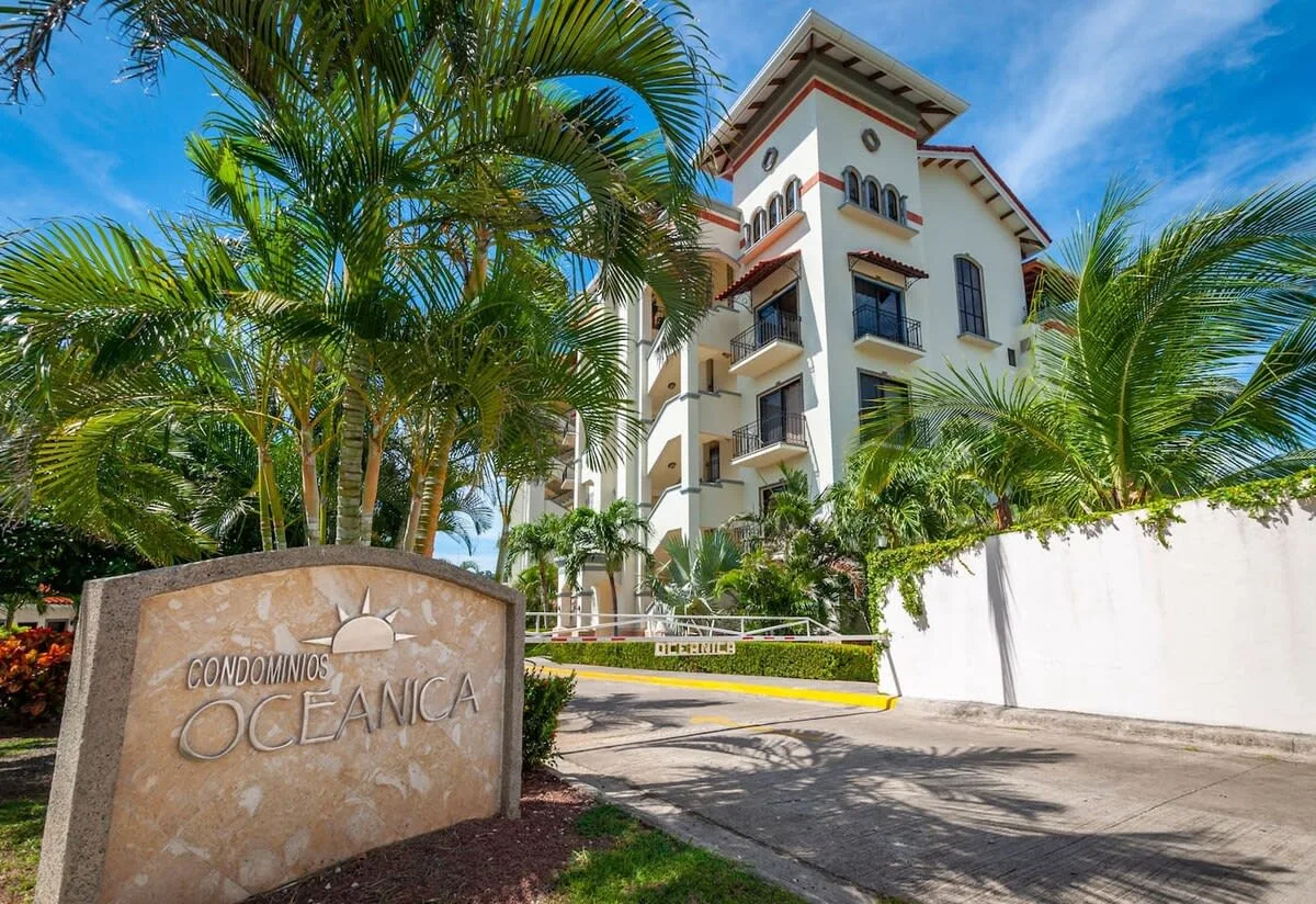 Shared amenity: A multi-story building stands behind palm trees beside a stone entrance sign.