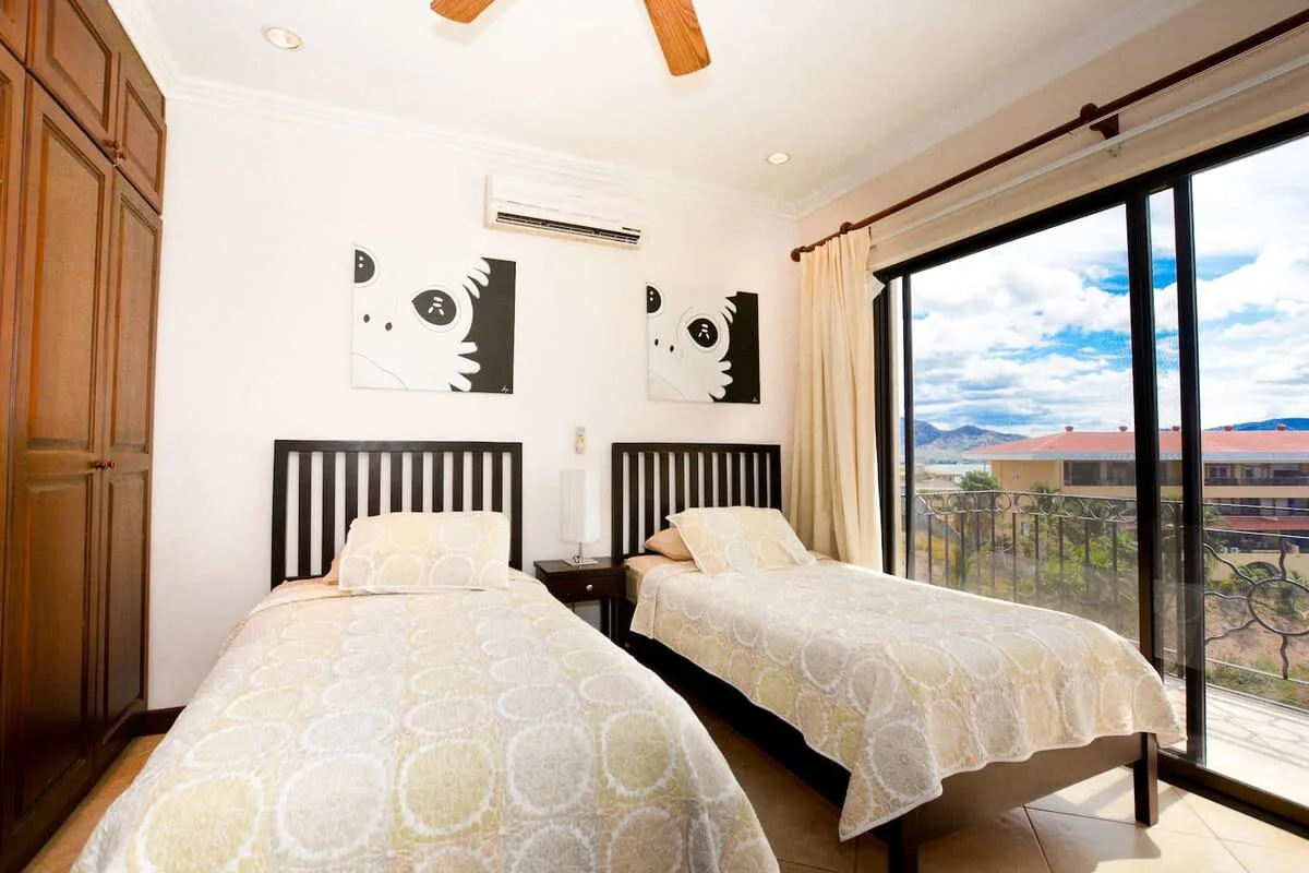 A bright bedroom with two beds beside a large sliding glass door.