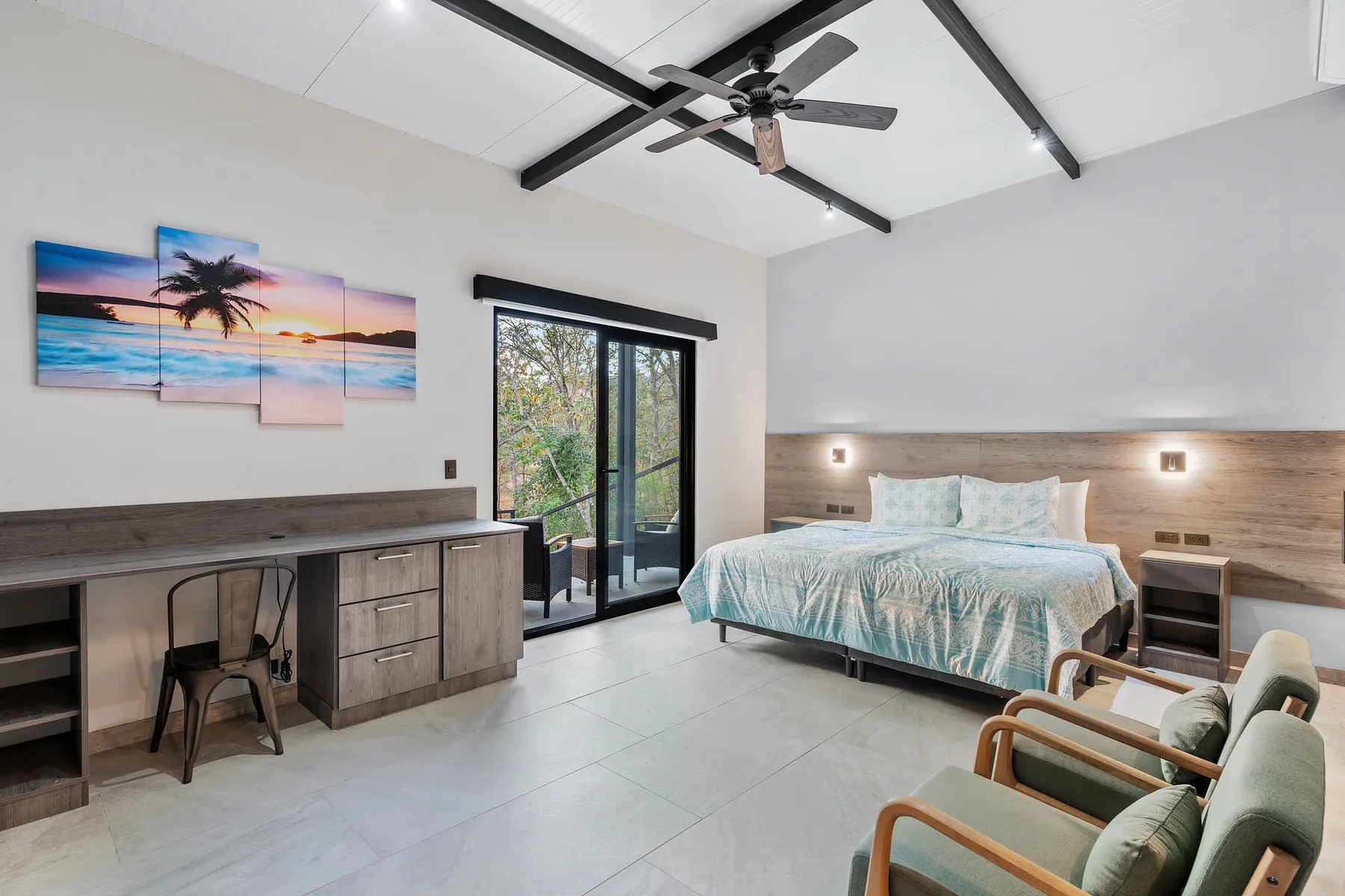 A bright bedroom with a bed, desk, and glass doors opening to greenery.