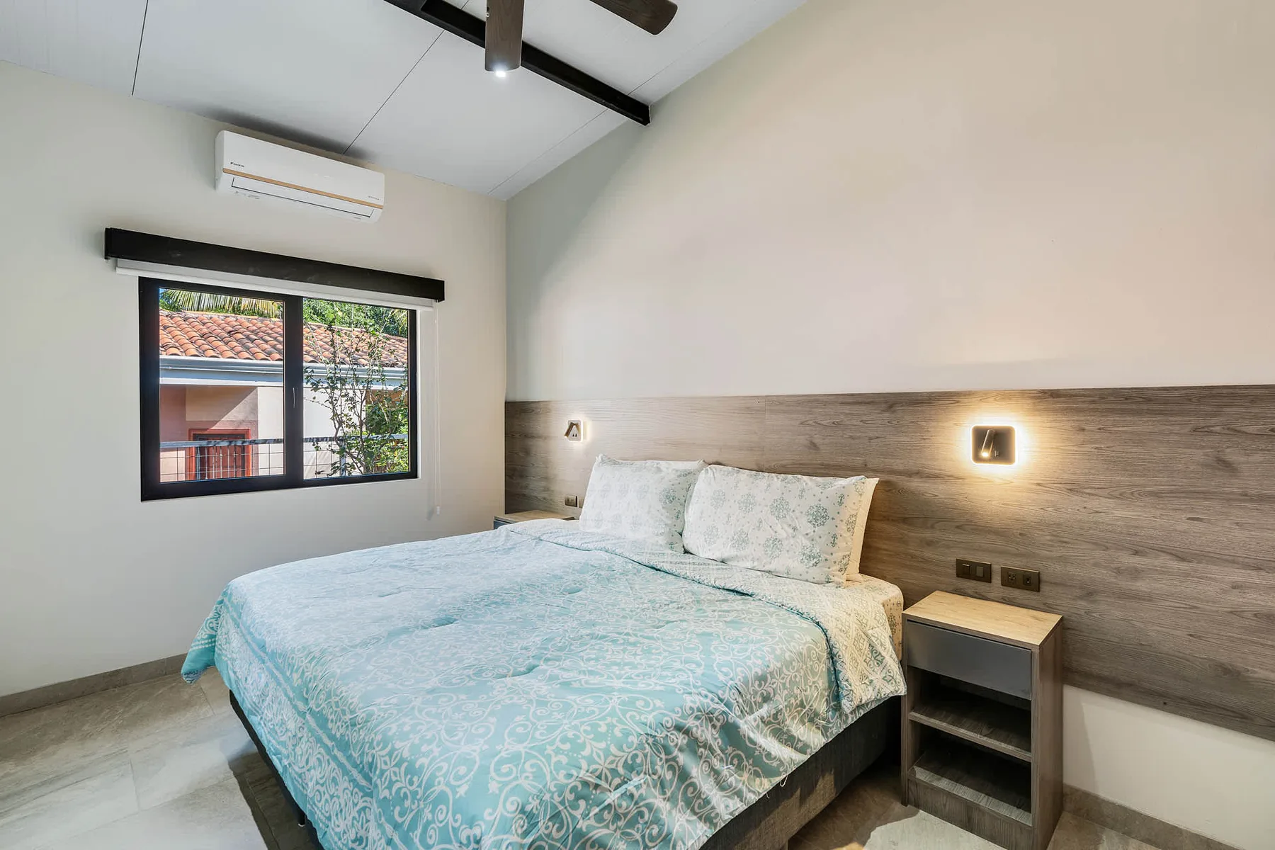 A bedroom with a bed beneath a wood-paneled headboard and a window.