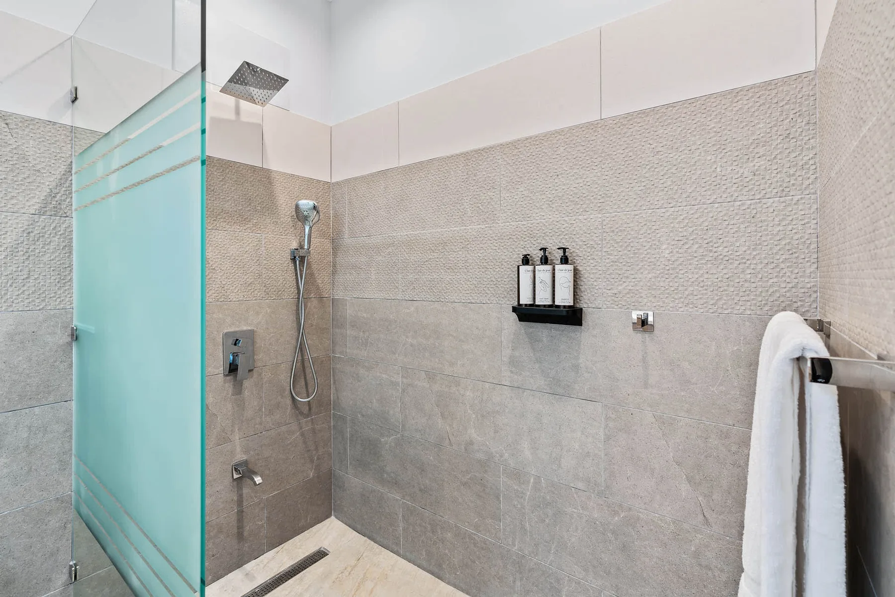 A tiled bathroom shower with a glass screen and wall-mounted dispensers.