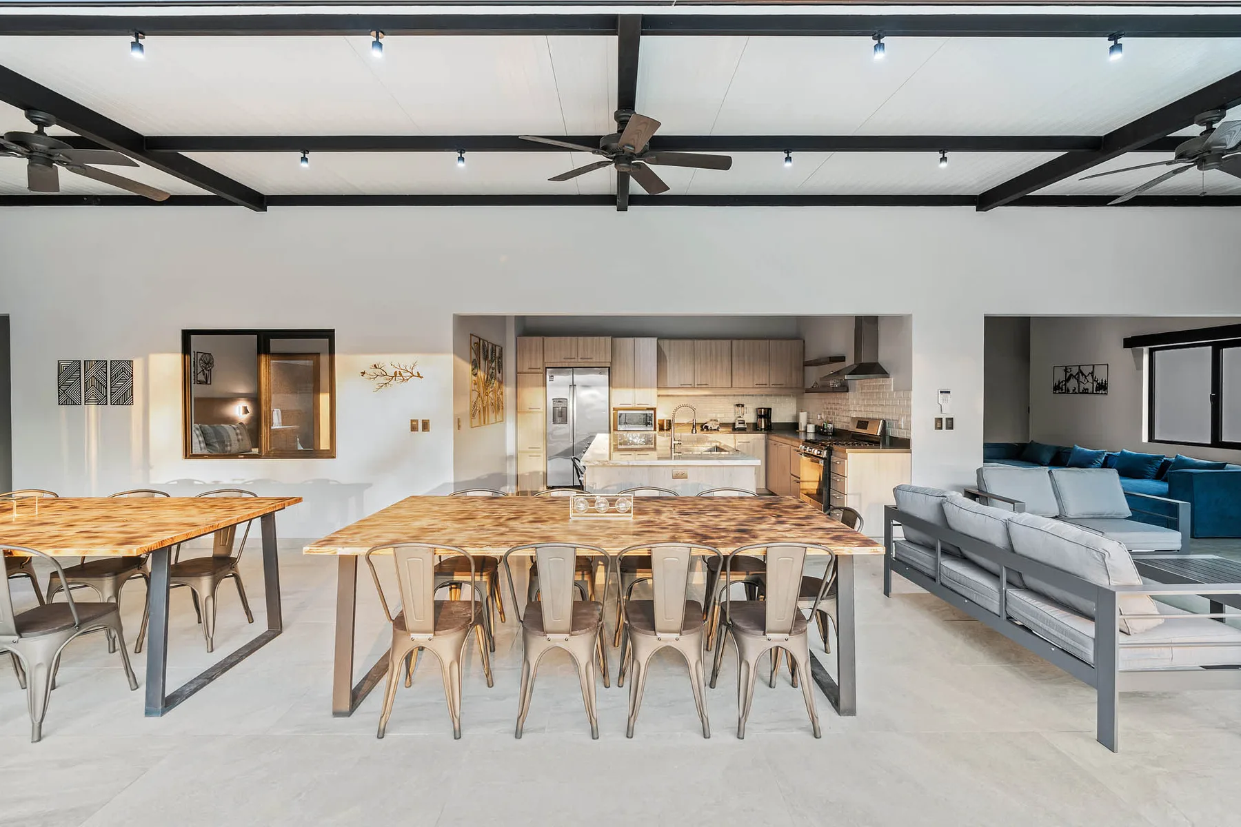 An open dining and living area with long tables, seating, and a kitchen in the background.