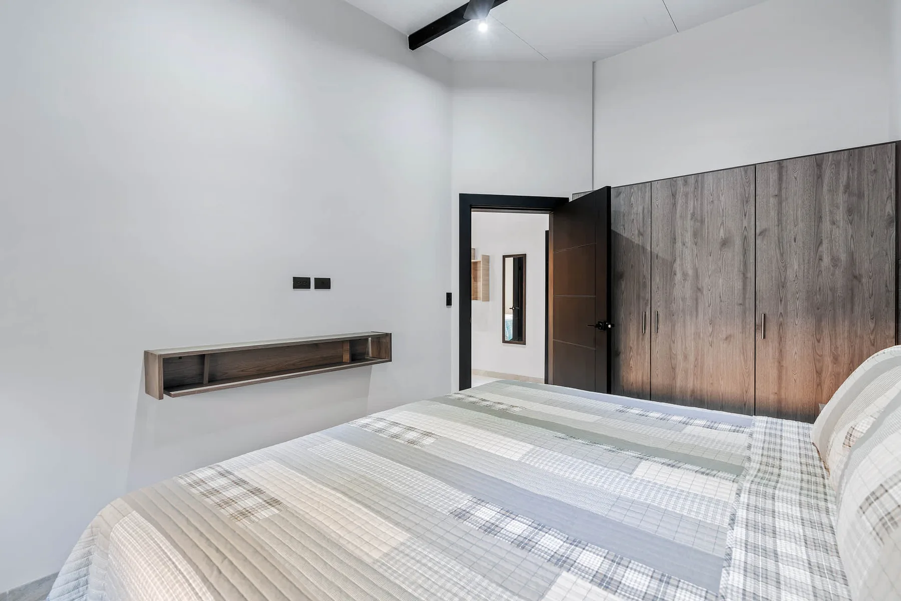 A bedroom with a bed beside a wood-paneled wall and an open doorway.