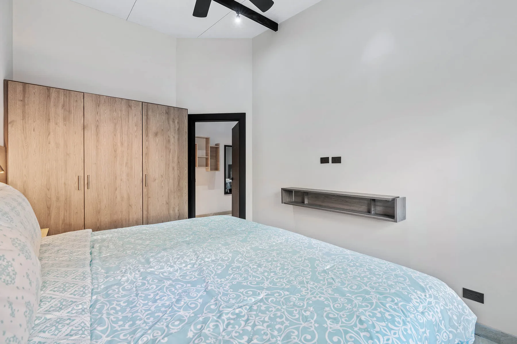 Bedroom with a patterned bedspread and a wooden wardrobe.