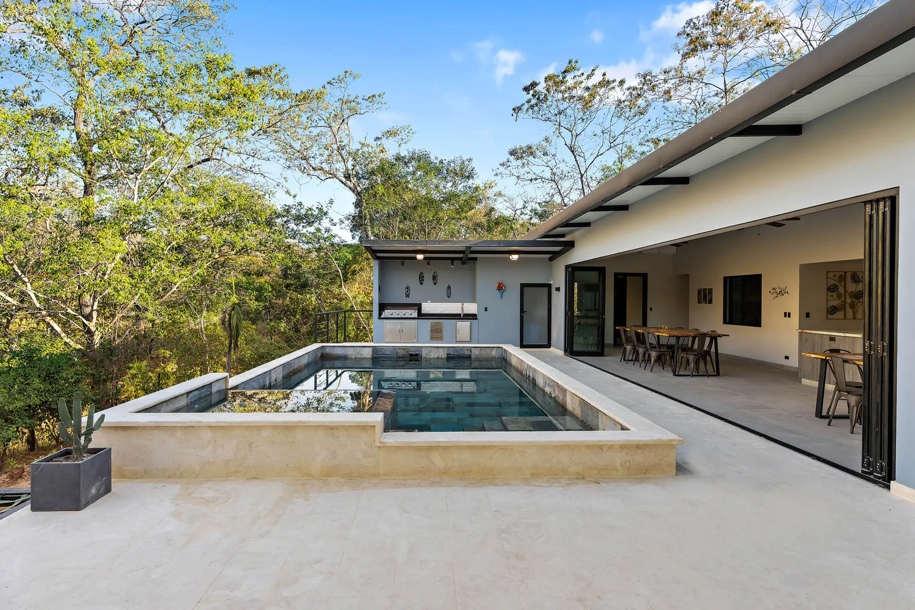An outdoor pool beside a covered dining area, surrounded by trees.