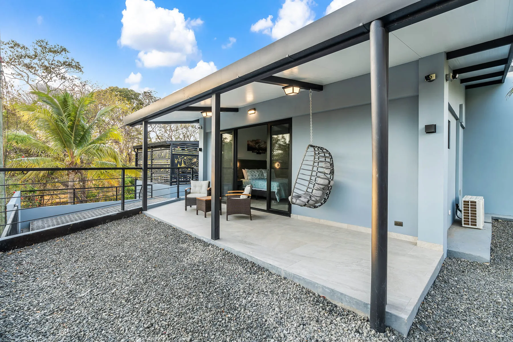 A covered outdoor patio with seating and a hanging chair overlooks trees.