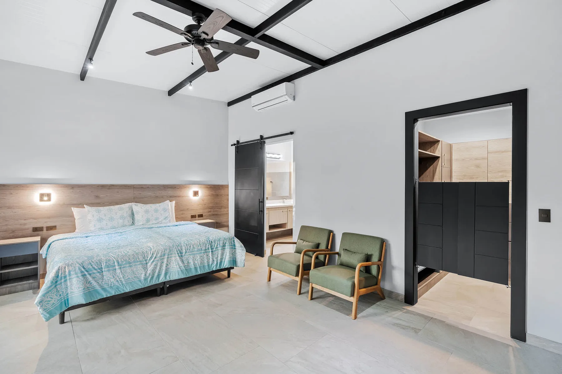 A bedroom with a bed and two chairs beside an open doorway.
