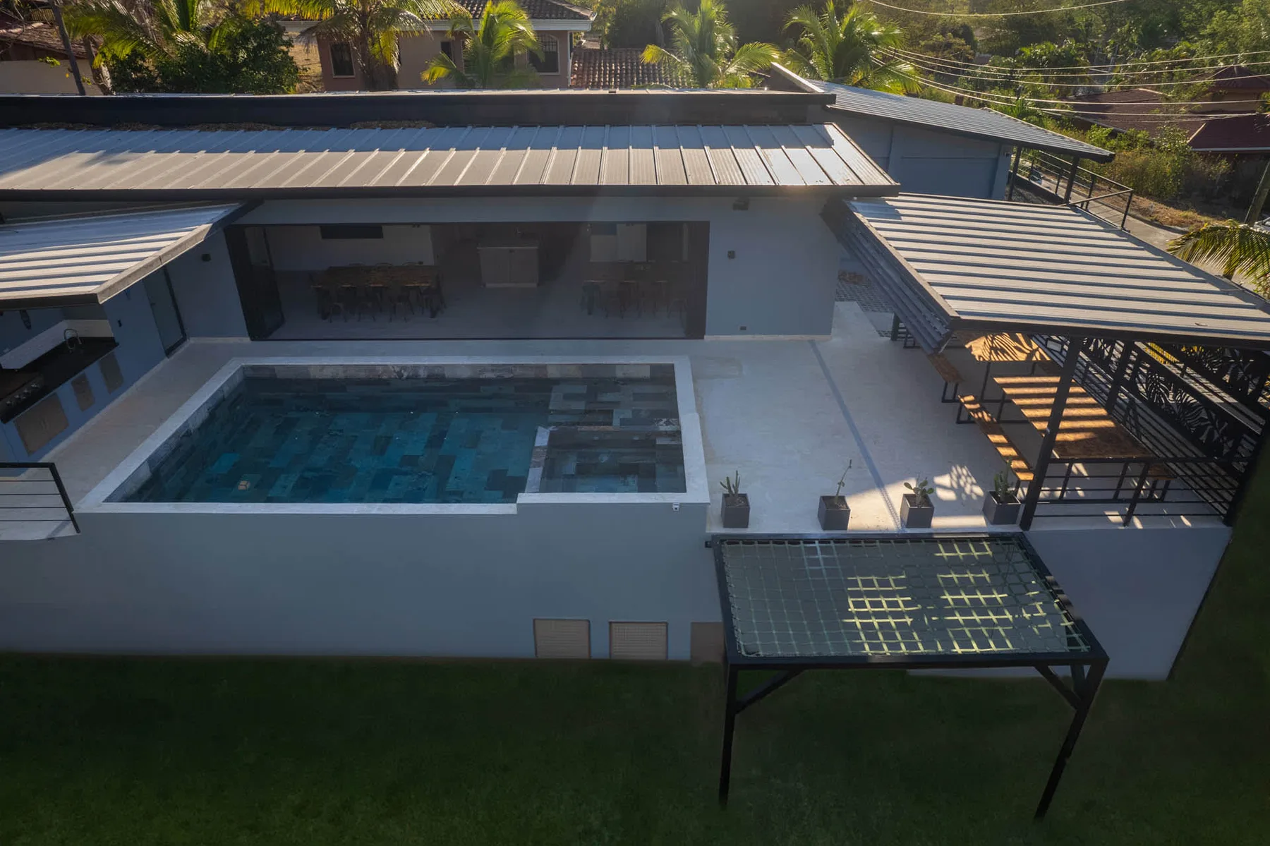 An aerial view of a modern house with a rectangular swimming pool and covered patio.