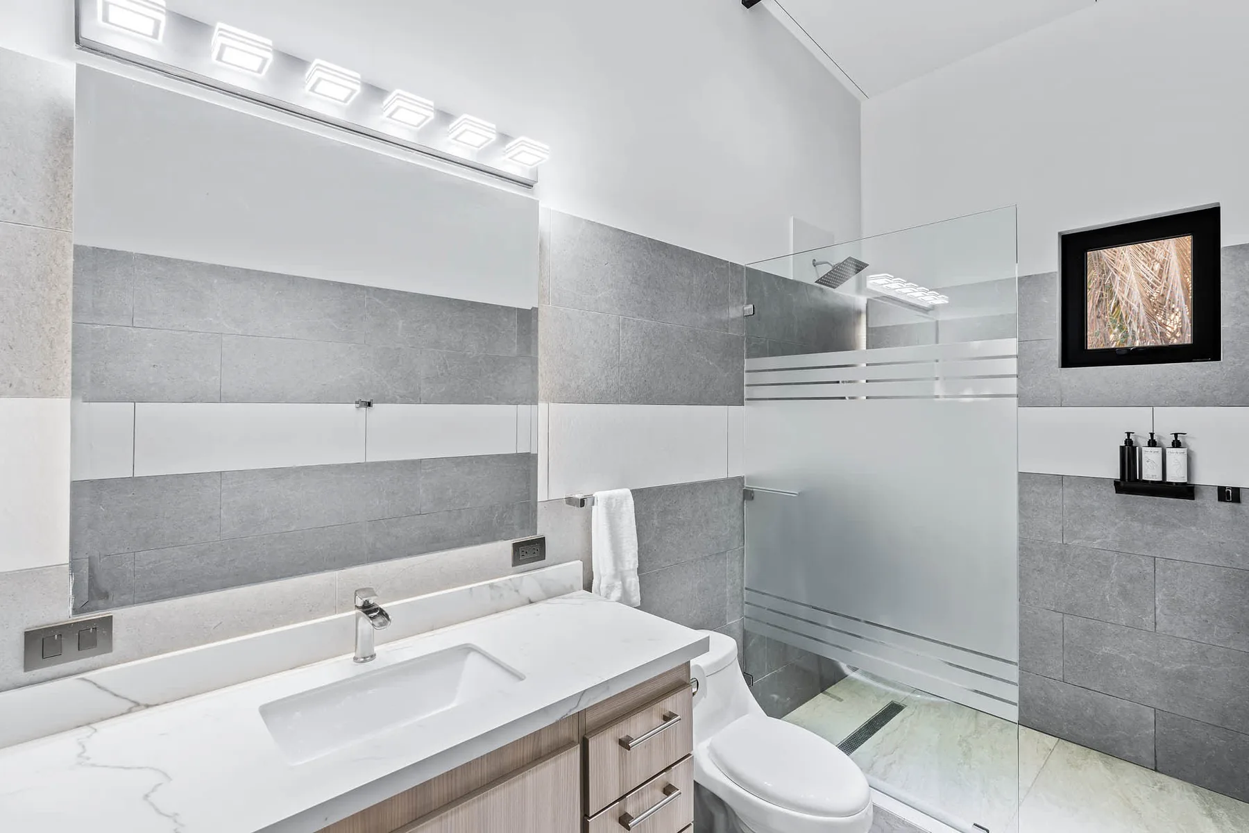 A modern bathroom with a wide vanity, toilet, and glass shower.