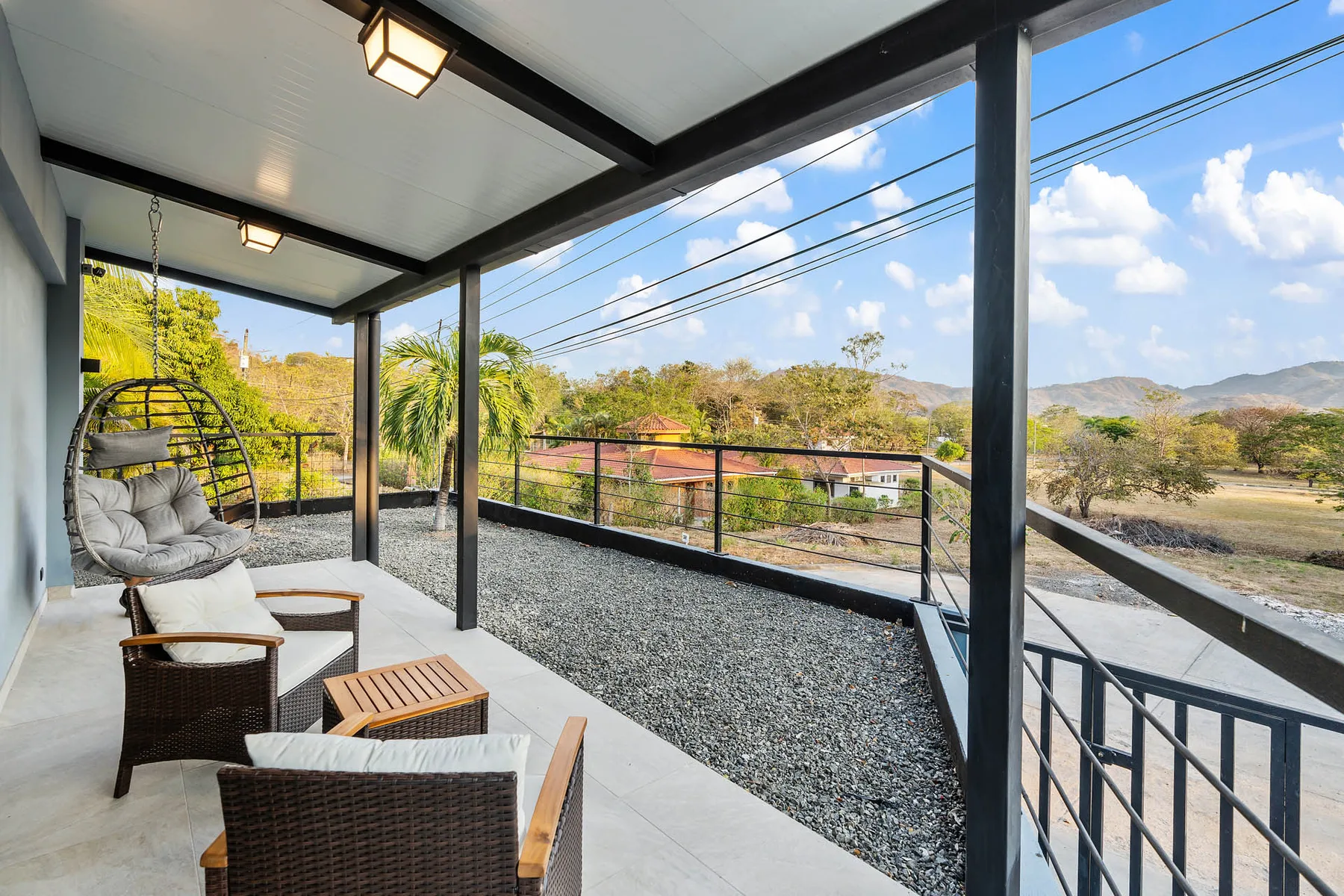 A covered outdoor patio with seating overlooks a green landscape and distant hills.