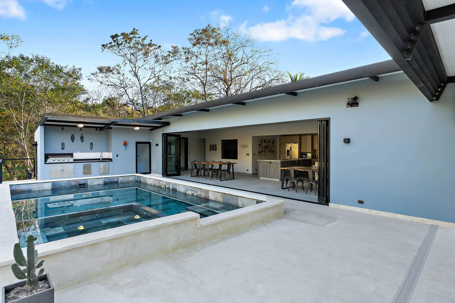 A modern outdoor kitchen and dining area opens onto a swimming pool.